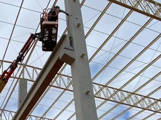 Técnico em plataforma elevatória junto aos pilares e às treliças da cobertura de um galpão