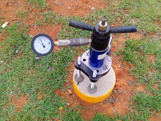 Equipamento de teste de carga com manômetro montado sobre um poste de ancoragem amarelo no gramado