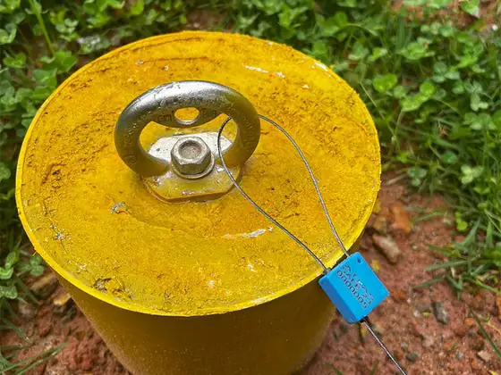 Olhal de ancoragem com lacre azul no topo de um poste amarelo, no gramado
