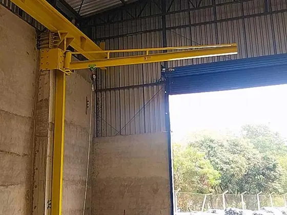 Braço giratório amarelo fixado em pilar junto ao portão de um galpão
