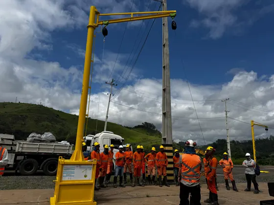 Pórtico com braço sobre base de contrapeso de concreto, equipe de uniforme laranja no pátio