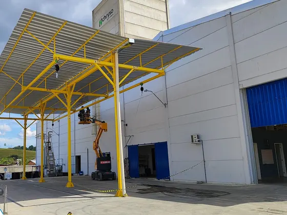 Pórtico fixo amarelo com cobertura sobre o pátio de carregamento, ao lado do galpão