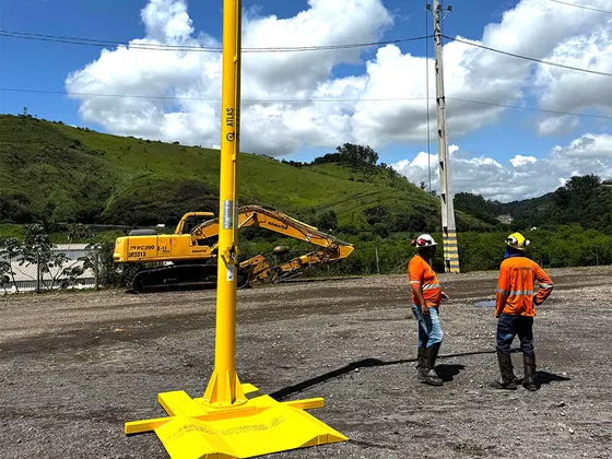 Pórtico com braço sobre base de pneu em pátio de terra, com dois trabalhadores ao lado