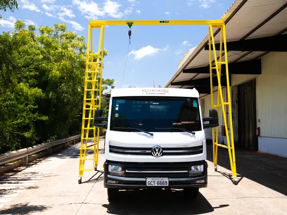Pórtico móvel tipo trave com escadas sobre um caminhão branco junto ao galpão