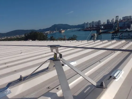 Interface trapezoidal inox sobre telhado metálico, com o porto e a cidade ao fundo